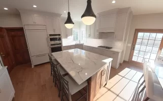 Amherst NY kitchen remodel with marble-look island, white shaker cabinets, double oven, and pendant lighting.