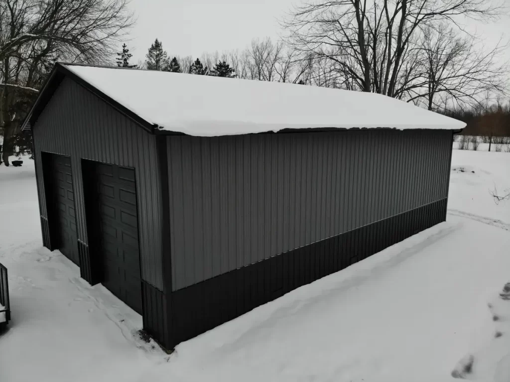 Frontal angle of a snow-covered Stately Pole Barn in East Amherst, NY, highlighting the large black garage doors.