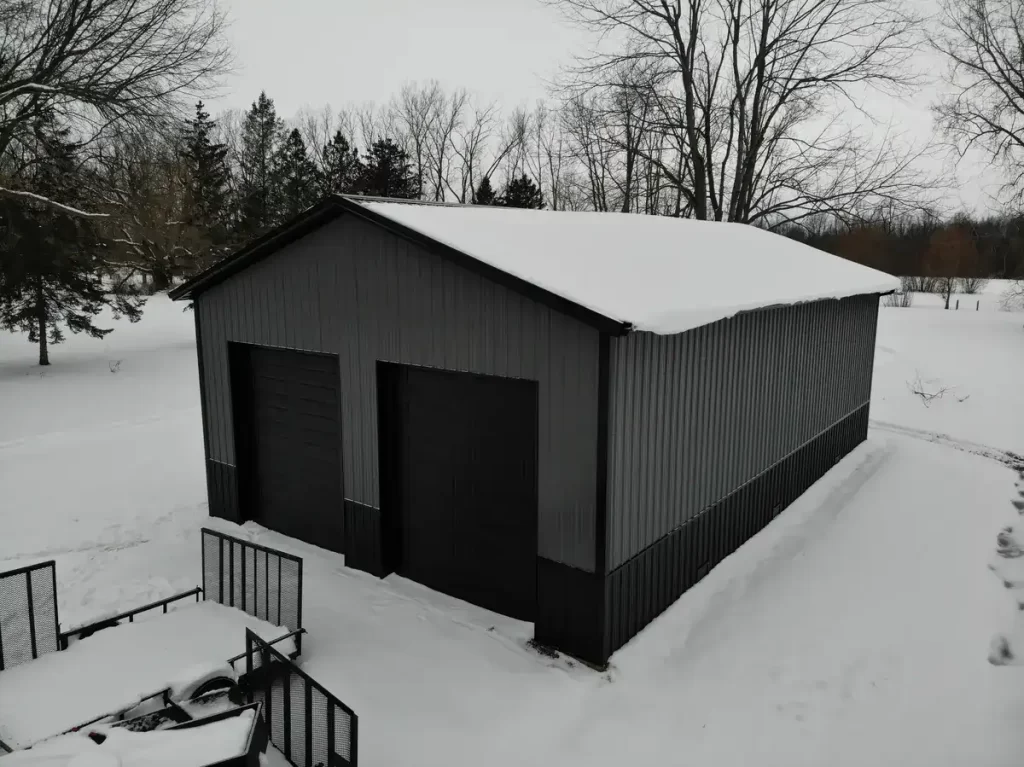 Frontal angle of a snow-covered Stately Pole Barn in East Amherst, NY, highlighting the large black garage doors.