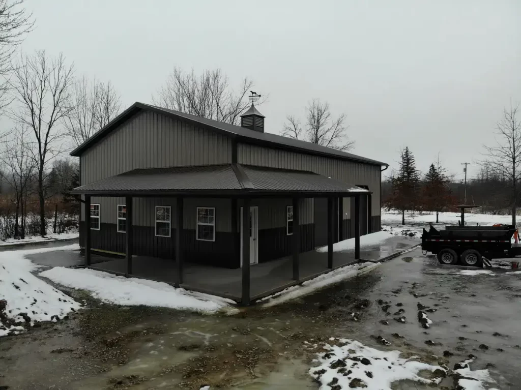 Front view of a pole barn with a cupola and weathervane, featuring large garage doors and windows, against a backdrop of overcast skies.