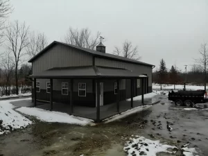Front view of a pole barn with a cupola and weathervane, featuring large garage doors and windows, against a backdrop of overcast skies.