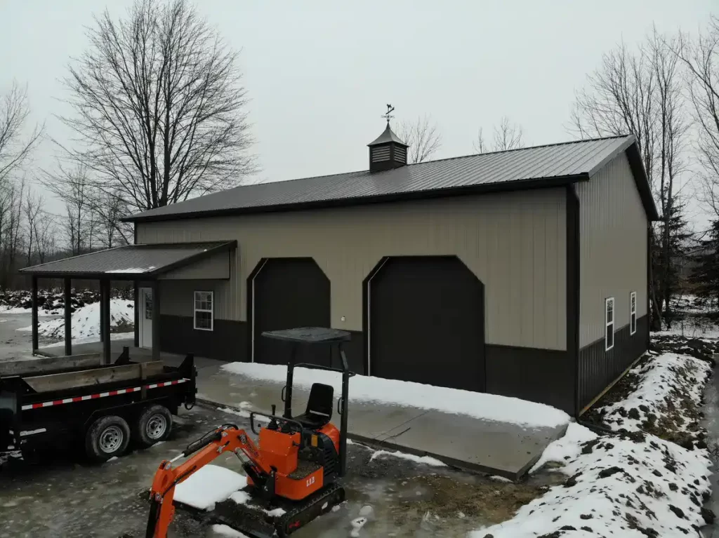 Angled view of a large pole barn with an attached lean-to, featuring several windows and garage doors, set against a snowy landscape."