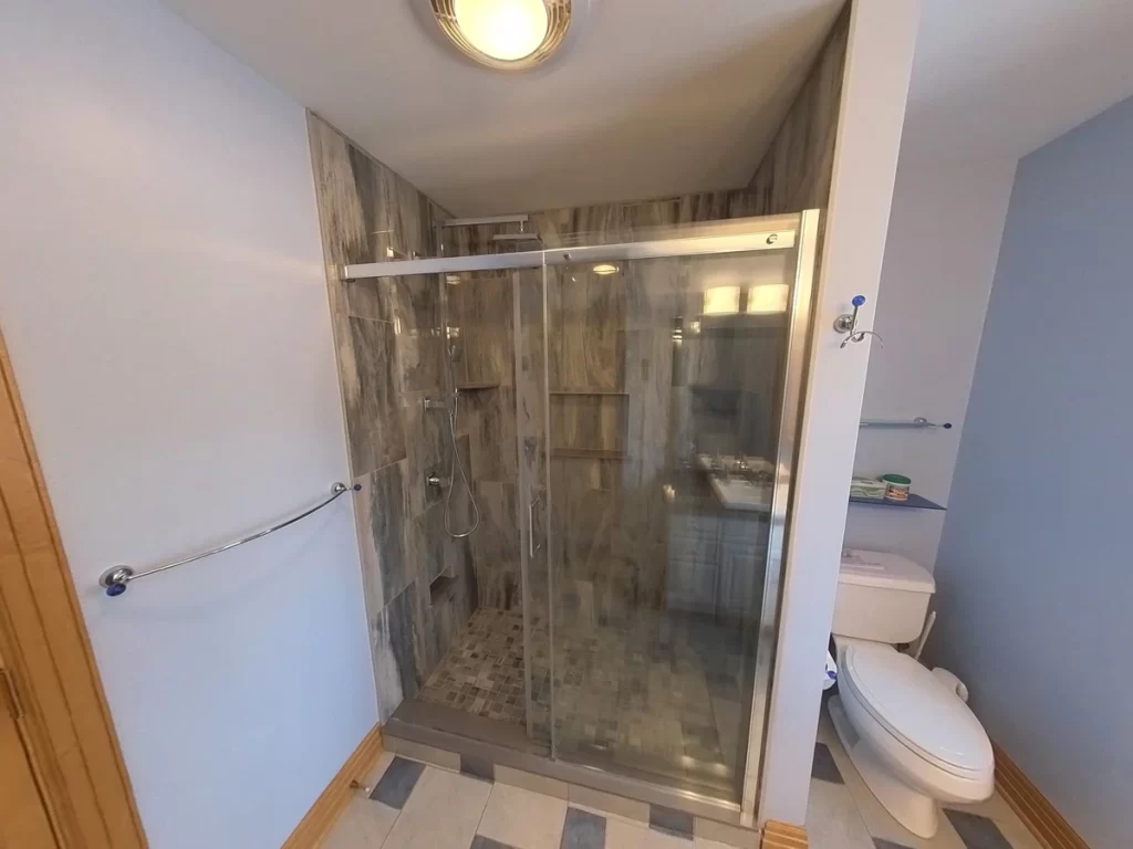 After renovation, an inviting walk-in shower with clear glass door, modern gray tile design, and high-quality fixtures is the centerpiece of this bathroom, highlighting the expertise of Stately Kitchen and Bath in delivering stylish and practical bathroom transformations.