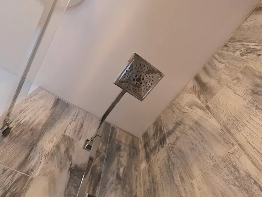 After renovation by Stately Kitchen and Bath: a luxury shower's high-end chrome square rain showerhead, accentuating the stylish gray marble tile work in the modern bathroom, enhancing the shower experience with a focus on sophisticated design.