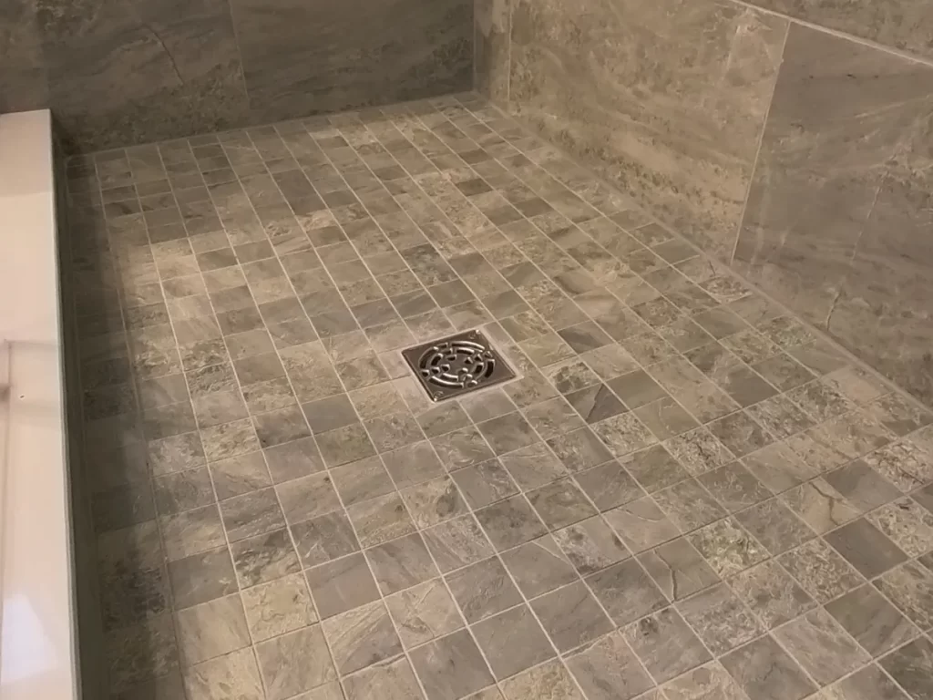 Finished tile flooring in a shower renovation with detailed stonework pattern and a central drain, part of Stately Kitchen and Bath's bathroom remodeling services.