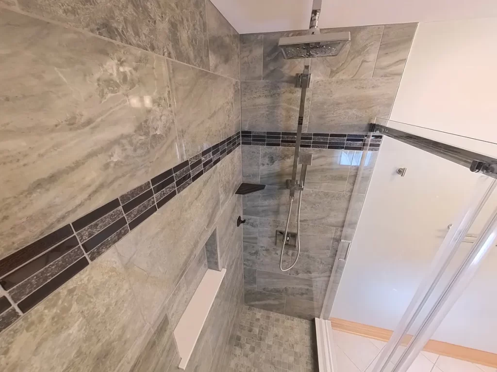 A top-down view of a newly transformed shower by Stately Kitchen and Bath with a wide showerhead, multi-function hand sprayer, and a custom tile pattern with a mosaic border, reflecting high-end bathroom upgrades for a contemporary home.