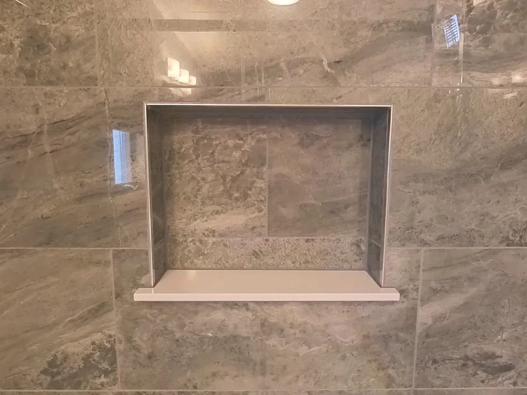Close-up view of a sleek, built-in shower niche in a newly renovated bathroom by Stately Kitchen and Bath, featuring marbled wall tiles and a clean, modern design for functional bathroom storage.