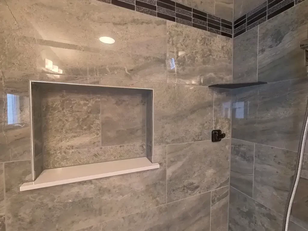 Elegant bathroom shower renovation by Stately Kitchen and Bath, showcasing a large marble-tiled wall with a spacious shower niche and a modern, wall-mounted square shower head for a luxurious home spa experience.
