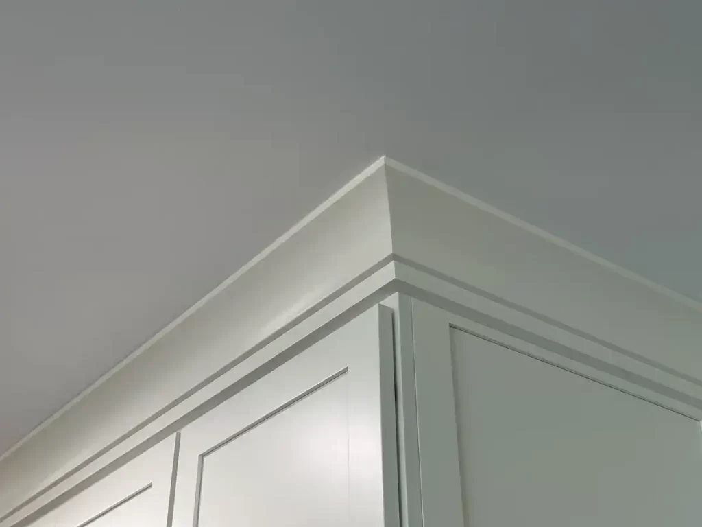 Detailed view of the precise and elegant crown molding trim work on white kitchen cabinets in a Stately Builders' kitchen remodel in Clarence, NY.