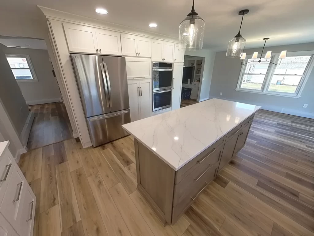 Elegant newly remodeled kitchen in Clarence, NY with large island, pendant lighting, hardwood floors, and modern stainless steel appliances by Stately Builders.