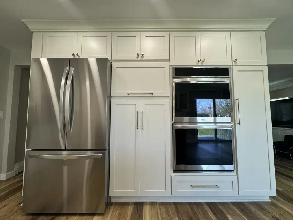 Clarence, NY kitchen remodel showcasing stainless steel French door refrigerator and double wall ovens set in white custom cabinetry by Reusch Woodworking. Designed and constructed by Stately Kitchen & Bath.