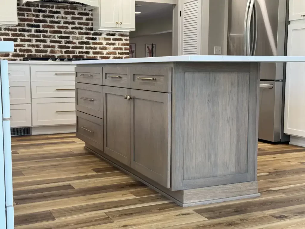 Custom maple island cabinetry with brass handles in a remodeled Clarence, NY kitchen, featuring exposed brick backsplash and hardwood flooring by Stately Kitchen & Bath.