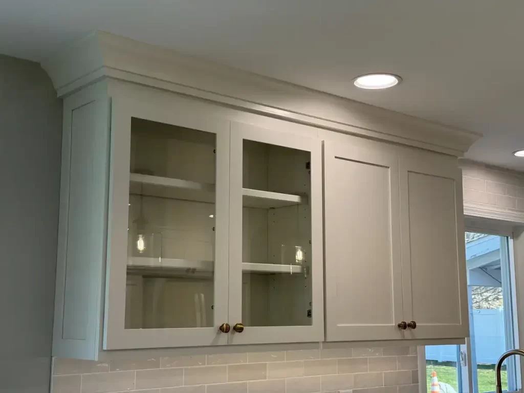 Finished kitchen remodel in Clarence, NY featuring upper cabinets with glass inserts by Reusch Woodworking, accented with brass knobs and under-cabinet lighting.