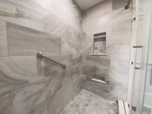Modern shower area with marble tile and built-in shelving in a bathroom remodel by Stately Kitchen and Bath in Gettzville, NY, featuring a grab bar for safety.