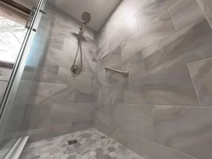 Elegant shower with marble tile and rain shower head in a bathroom remodel by Stately Kitchen and Bath in Gettzville, NY, featuring a grab bar and hexagonal floor tiles.
