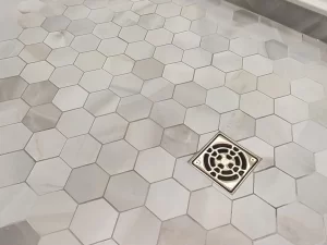 Close-up of hexagonal marble floor tiles and a decorative drain in the shower of a bathroom remodel by Stately Kitchen and Bath in Gettzville, NY.