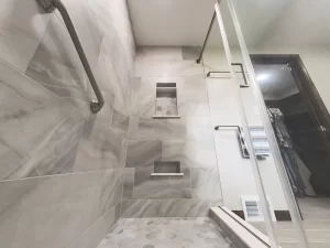 Shower area with built-in shelving, marble tile, and a grab bar in a bathroom remodel by Stately Kitchen and Bath in Gettzville, NY.