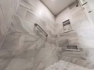 Elegant shower with marble tile, built-in shelving, and a grab bar in a bathroom remodel by Stately Kitchen and Bath in Gettzville, NY.