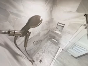 Overhead view of a shower with a rain shower head, marble tile, built-in shelving, and a grab bar in a bathroom remodel by Stately Kitchen and Bath in Gettzville, NY.