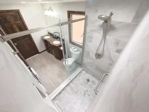 Overhead view of a modern bathroom remodel by Stately Kitchen and Bath in Gettzville, NY, featuring a glass-enclosed shower, double vanity with granite countertops, and a rain shower head.