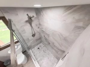 Overhead view of a shower with marble tile, rain shower head, and grab bar in a bathroom remodel by Stately Kitchen and Bath in Gettzville, NY.
