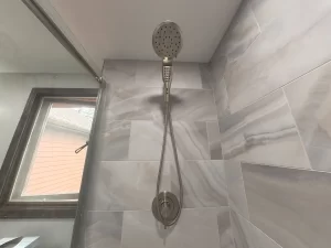 Close-up of a rain shower head with marble tile backdrop in a bathroom remodel by Stately Kitchen and Bath in Gettzville, NY.