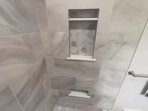 Detail of built-in shelving with hexagonal tile in the shower of a bathroom remodel by Stately Kitchen and Bath in Gettzville, NY.