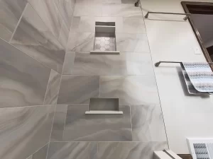 Built-in shelving and marble tile in the shower area of a bathroom remodel by Stately Kitchen and Bath in Gettzville, NY, with modern fixtures.