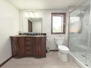 Modern bathroom remodel by Stately Kitchen and Bath in Gettzville, NY, featuring a double vanity with granite countertops, large mirror, and glass-enclosed shower.