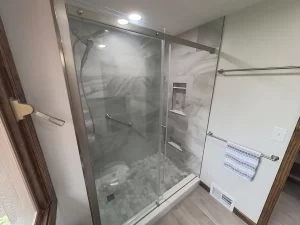 Detail of a modern shower in a bathroom remodel by Stately Kitchen and Bath in Gettzville, NY, featuring a glass enclosure, built-in shelving, and elegant marble tile.