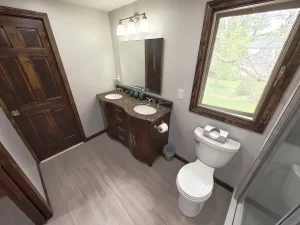 Modern bathroom remodel in Gettzville, NY by Stately Kitchen and Bath, highlighting a double vanity with granite countertops, a large mirror, and natural light from a window.