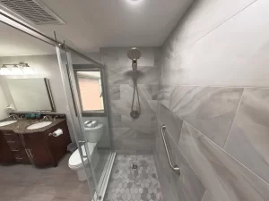 Elegant bathroom remodel by Stately Kitchen and Bath in Gettzville, NY, featuring a glass-enclosed shower with marble tile, rain shower head, and a double vanity with granite countertops.