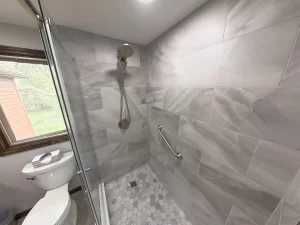 Close-up of the shower area in a bathroom remodel by Stately Kitchen and Bath in Gettzville, NY, featuring marble tile, rain showerhead, and a built-in grab bar.
