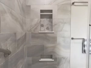 Detail of built-in shelving in the shower area of a bathroom remodel by Stately Kitchen and Bath in Gettzville, NY, featuring marble tile and modern fixtures.