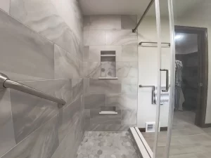 Shower area in a bathroom remodel by Stately Kitchen and Bath in Gettzville, NY, showcasing marble tile, built-in shelving, and a grab bar.
