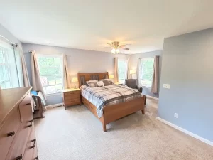 Clarence, NY home addition by Stately General Contracting, showcasing the primary bedroom suite with elegant furniture and large windows.