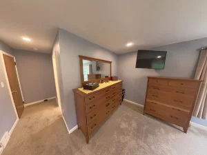 Clarence, NY home addition by Stately General Contracting, showing the primary bedroom suite with dresser, TV, and bright interior design.