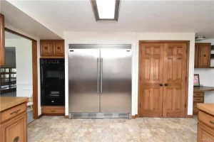Old kitchen with large stainless steel refrigerator and wooden pantry doors.