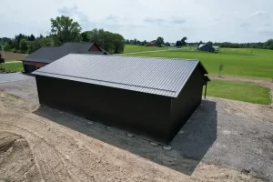 Angled aerial view of a matte black 40x60 pole barn in Clarence, NY, highlighting the solid construction and seamless integration with the surrounding landscape.