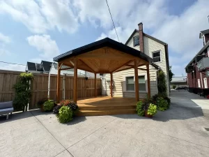 Wooden soundstage in Buffalo Olde Brewing beer garden, surrounded by seating and planters, designed for live music and events.