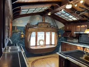 Wide-angle view of the ship-themed kitchen in Elma, NY, before remodel, featuring a faux ship stern and dark wood accents.