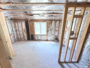 Bathroom demolition phase showing exposed wall studs and insulation, with a window still intact.