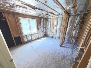 Bathroom stripped down to the studs during the demolition process, with a view of the window and ventilation ducts.
