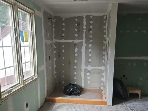 Bathroom build-out phase showing a partially finished shower alcove with GoBoard waterproofing and a large window next to it.