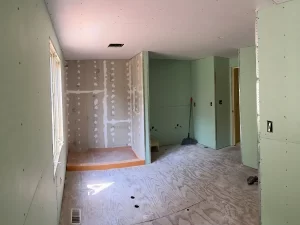 Bathroom build-out with drywall installation nearing completion, featuring a shower area and plywood flooring.