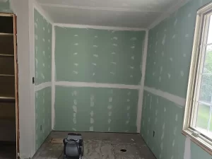 Partially finished bathroom build-out showing drywall installation with a greenboard wall for moisture protection.