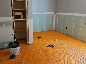 Radiant heated flooring system installed with orange underlayment, ready for tile installation in the bathroom build-out.