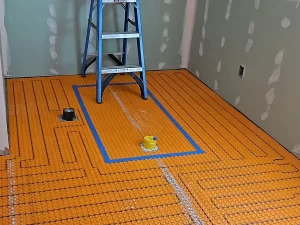 Radiant heated flooring system installation with orange underlayment, covering the bathroom floor in preparation for tile.