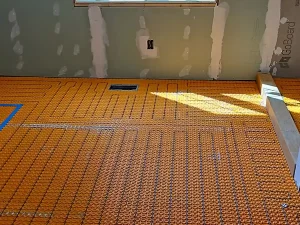 Radiant heated flooring installation nearing completion, with orange underlayment and blue markings visible on the bathroom floor.