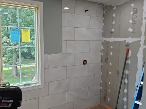 Shower wall with partially installed white subway tiles, next to a large window during the bathroom build-out.